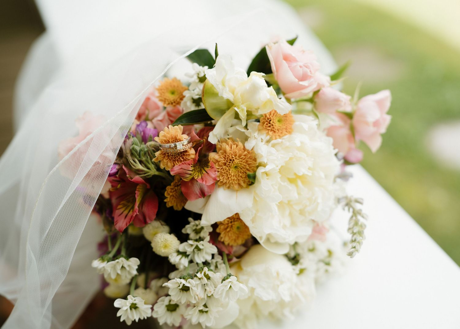 Beautiful bridal bouquet featuring white peonies, pink roses, and colorful wildflowers on a white surface.