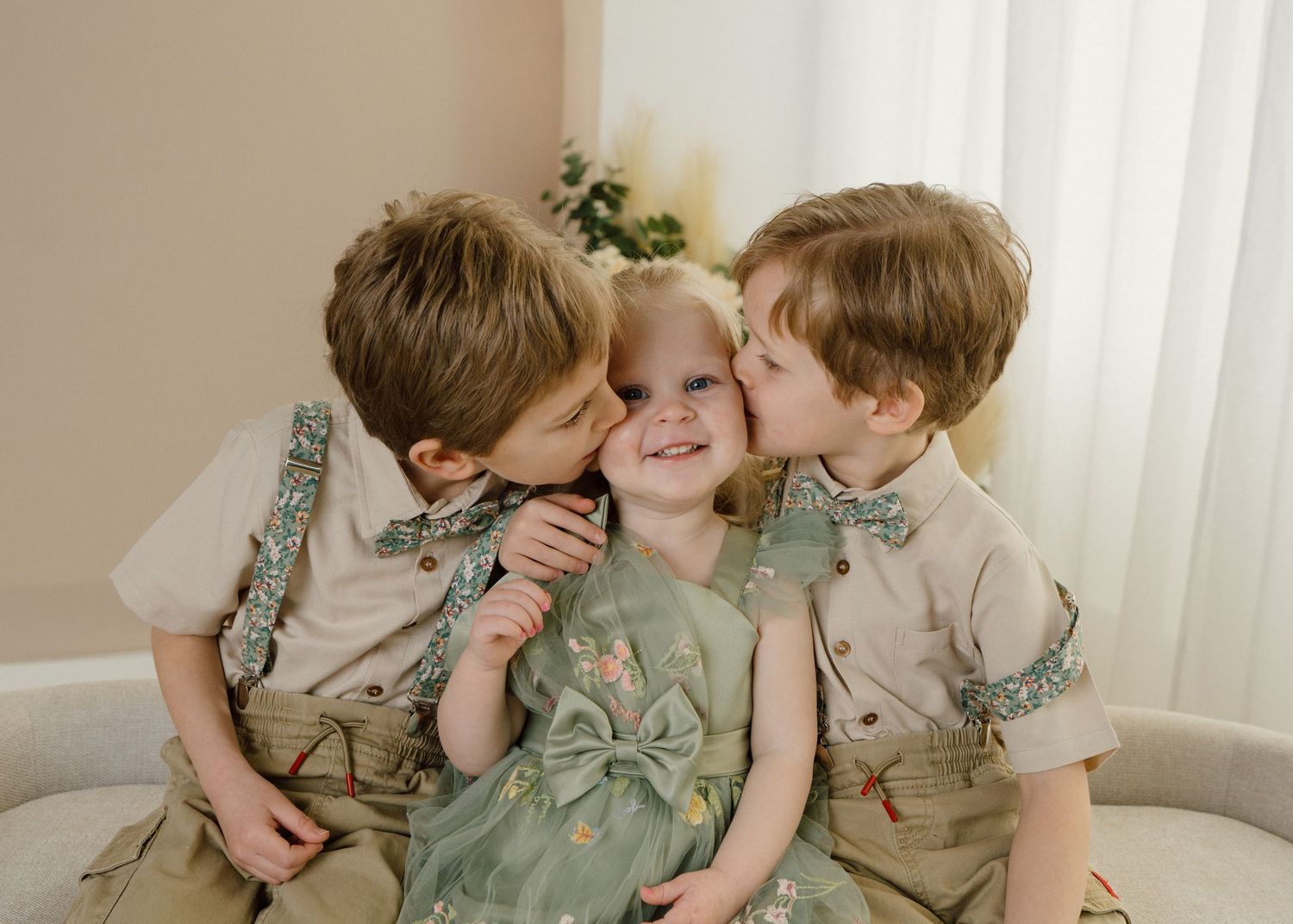 Two brothers kissing their smiling little sister on the cheeks during a sweet sibling portrait session.