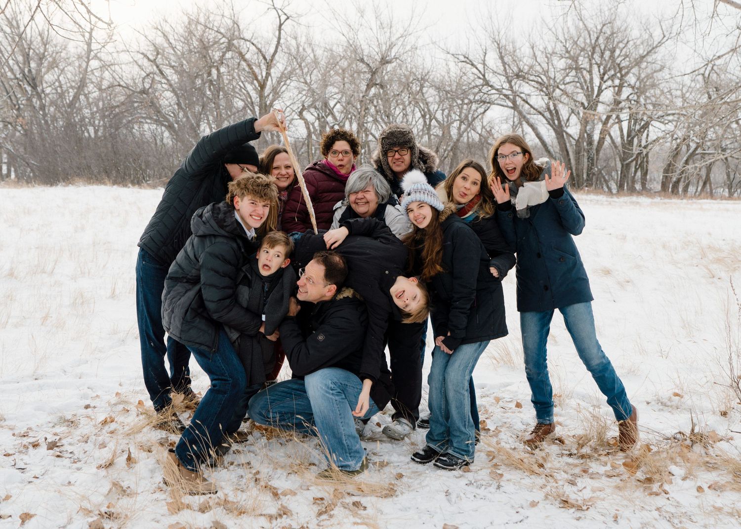 Large group of teens and young adults playfully posing together in snowy winter field.