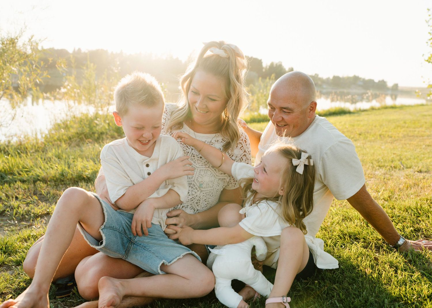 Happy family of five sitting together on green grass in warm sunset light.