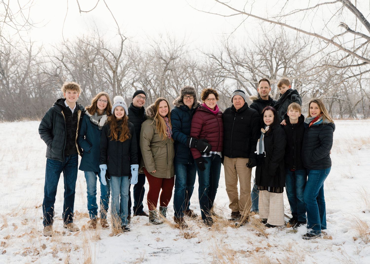 Large extended family group portrait standing together in snowy wooded winter landscape.