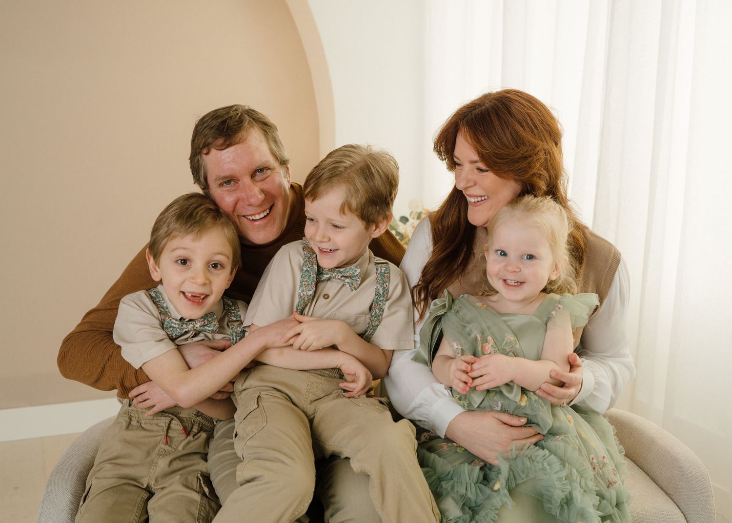 Happy family of five with parents and three young children smiling together during a studio family portrait.