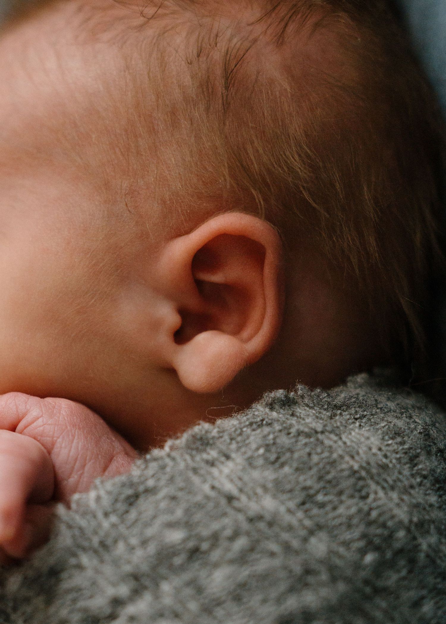 Close-up detail shot of newborn baby ear with fine hair and tiny fingers visible.