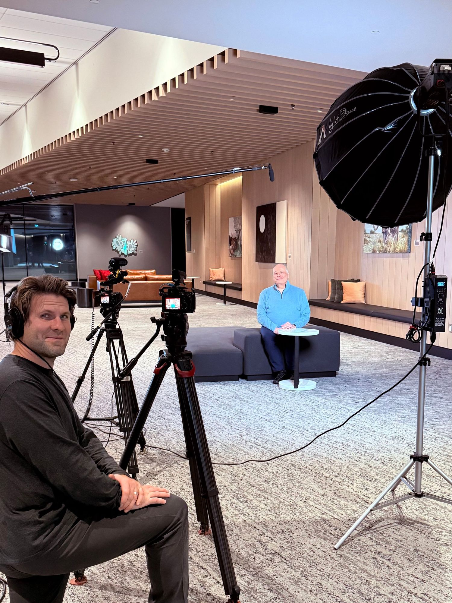 Videographer setting up camera equipment with professional lighting for an interview shoot in a modern office lobby.
