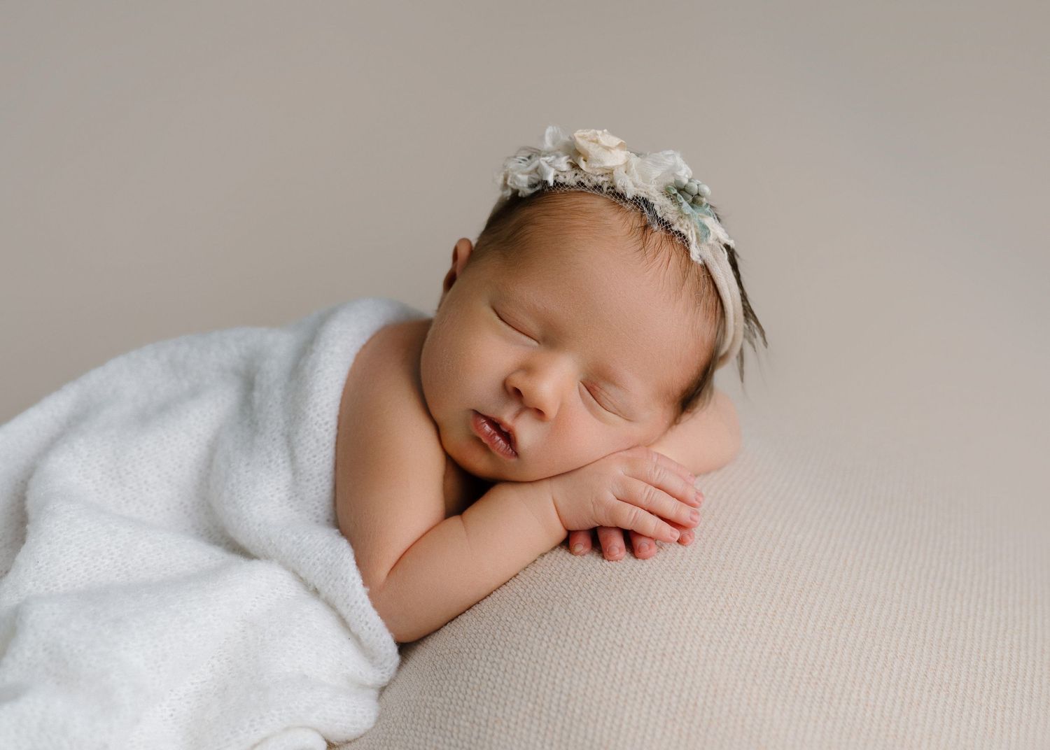 Sleeping newborn baby posed with hands under cheek on white blanket wearing a delicate floral headband.