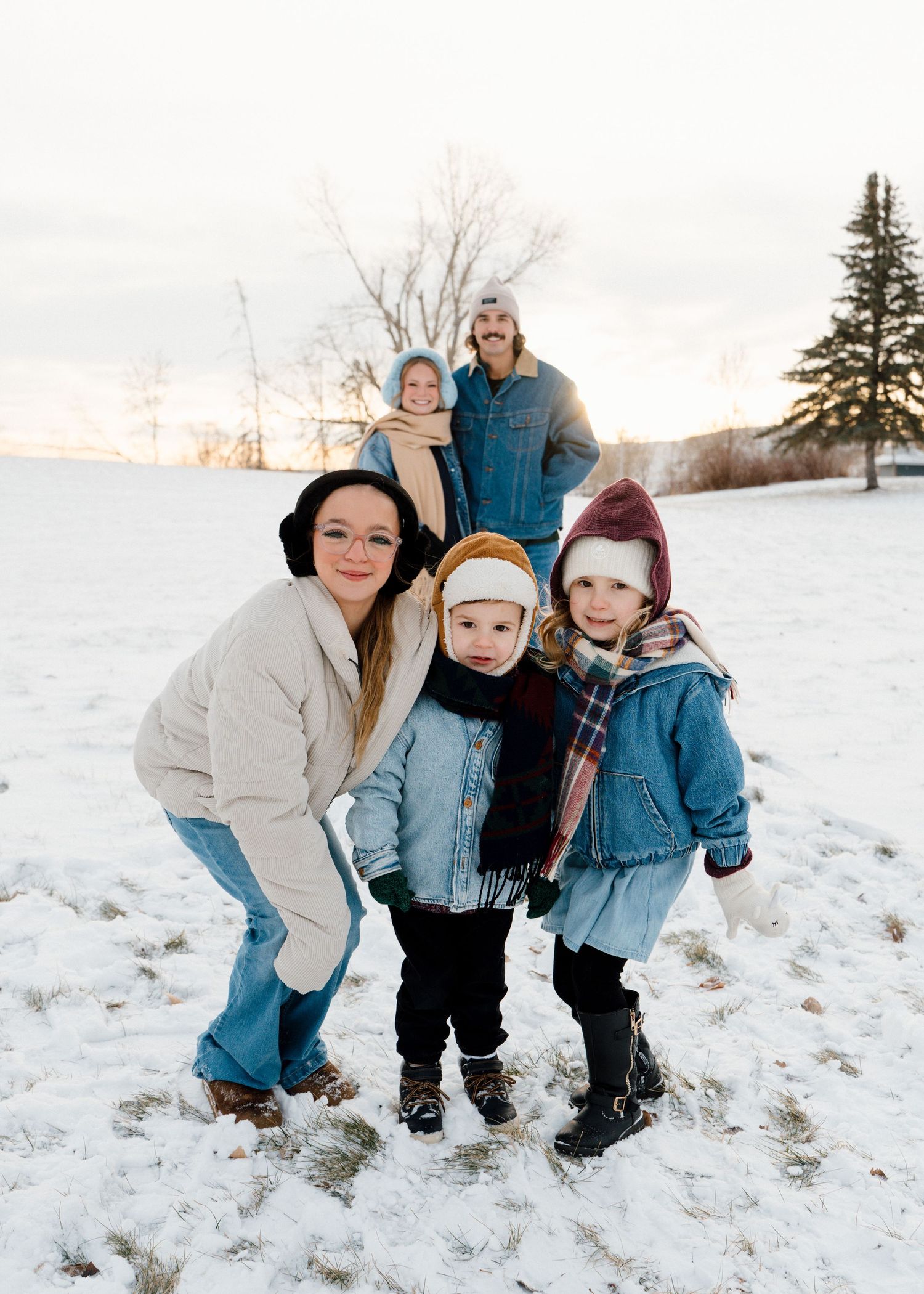 Family of five posing outdoors in snowy winter field wearing cozy scarves and winter coats.
