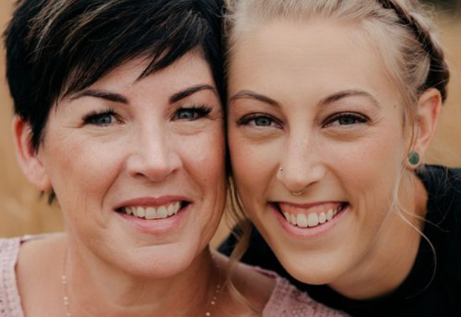 Two smiling women posing cheek to cheek in a warm outdoor portrait.