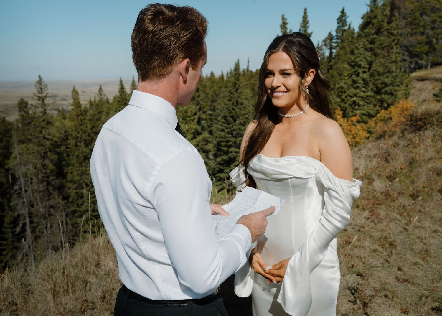 Bride and groom exchange vows on a mountain overlook surrounded by pine trees.