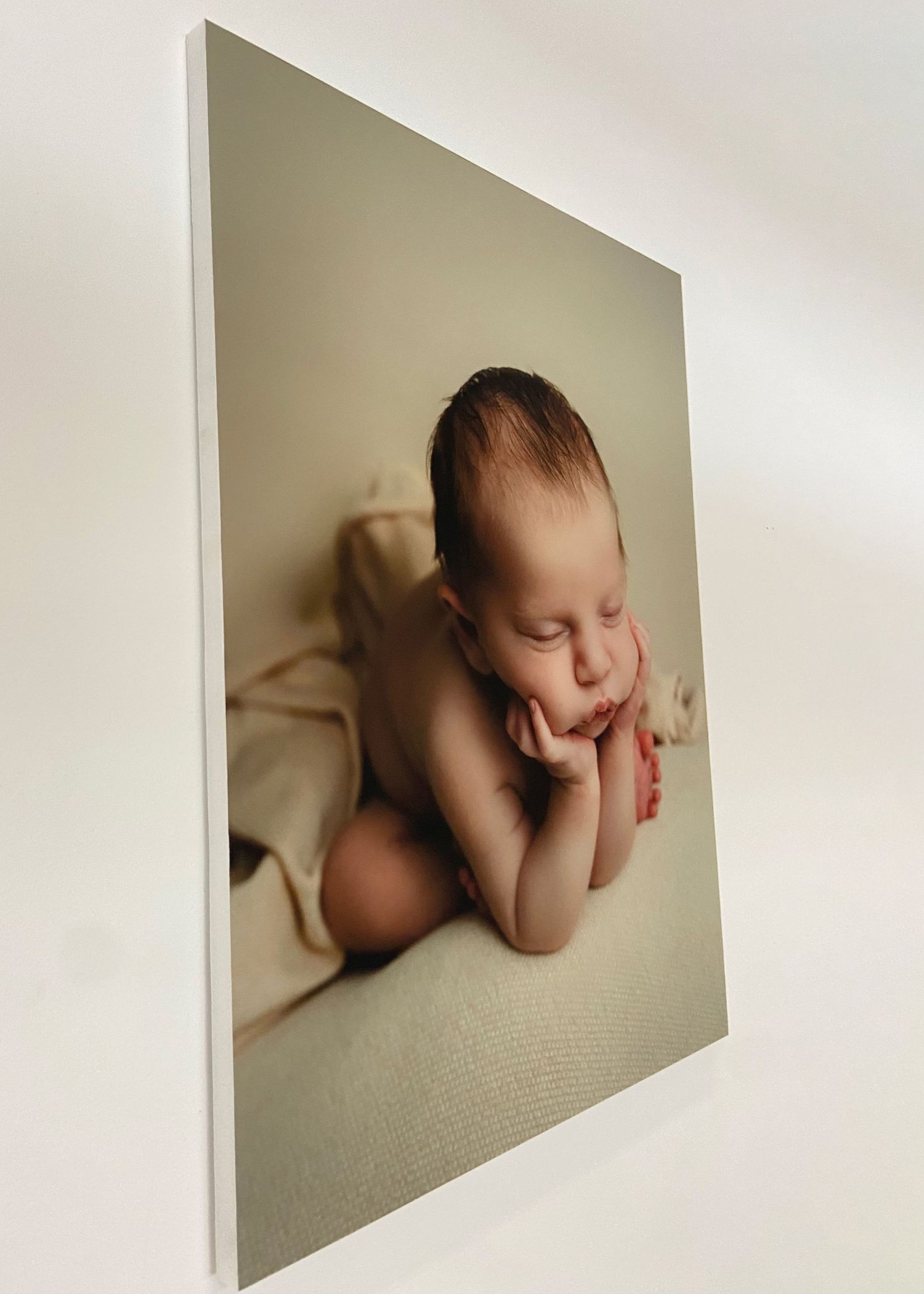 Professional newborn portrait print mounted on white foam board displayed on wall.