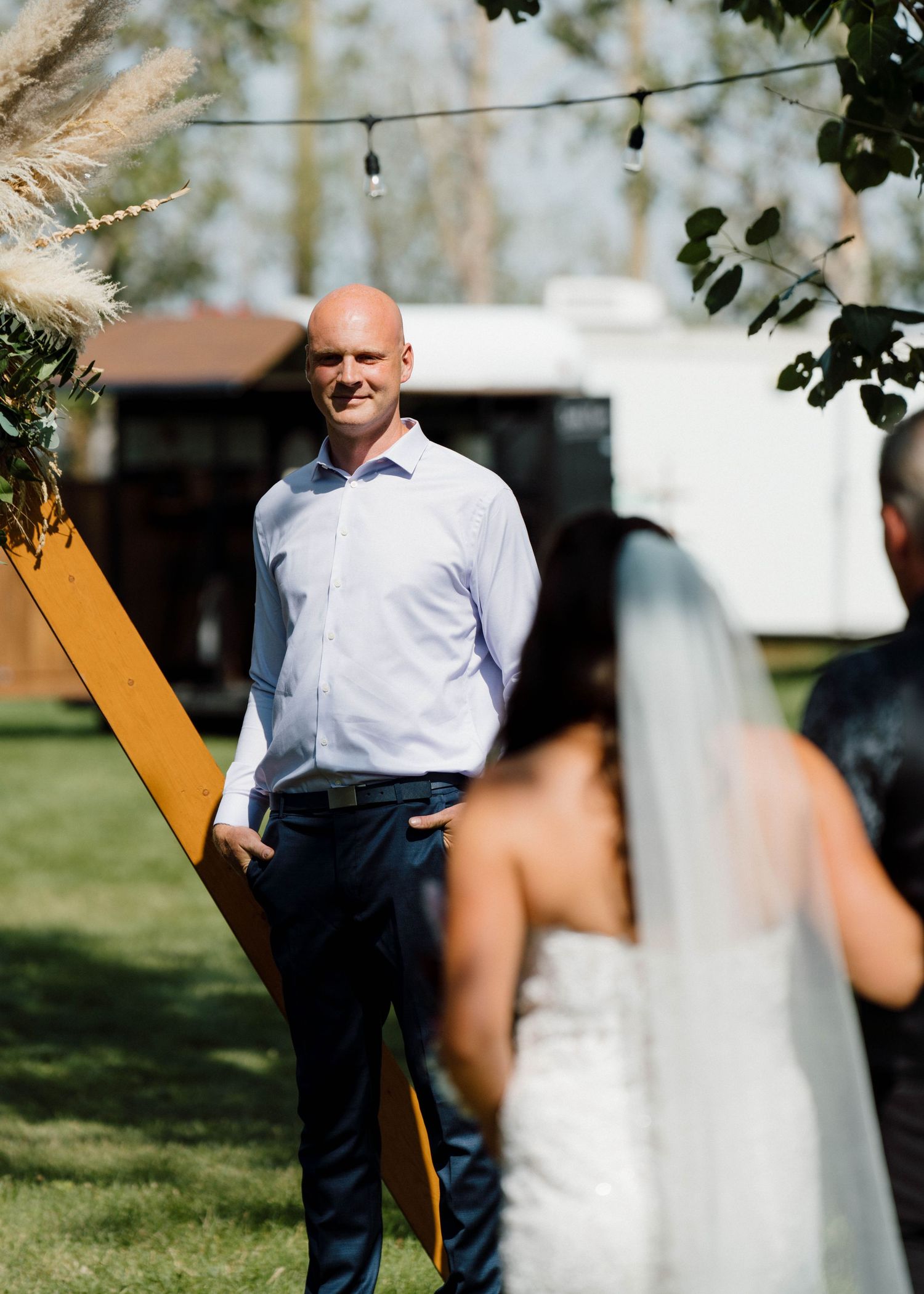 Groom watches with emotion as bride walks down the aisle at an outdoor wedding ceremony.