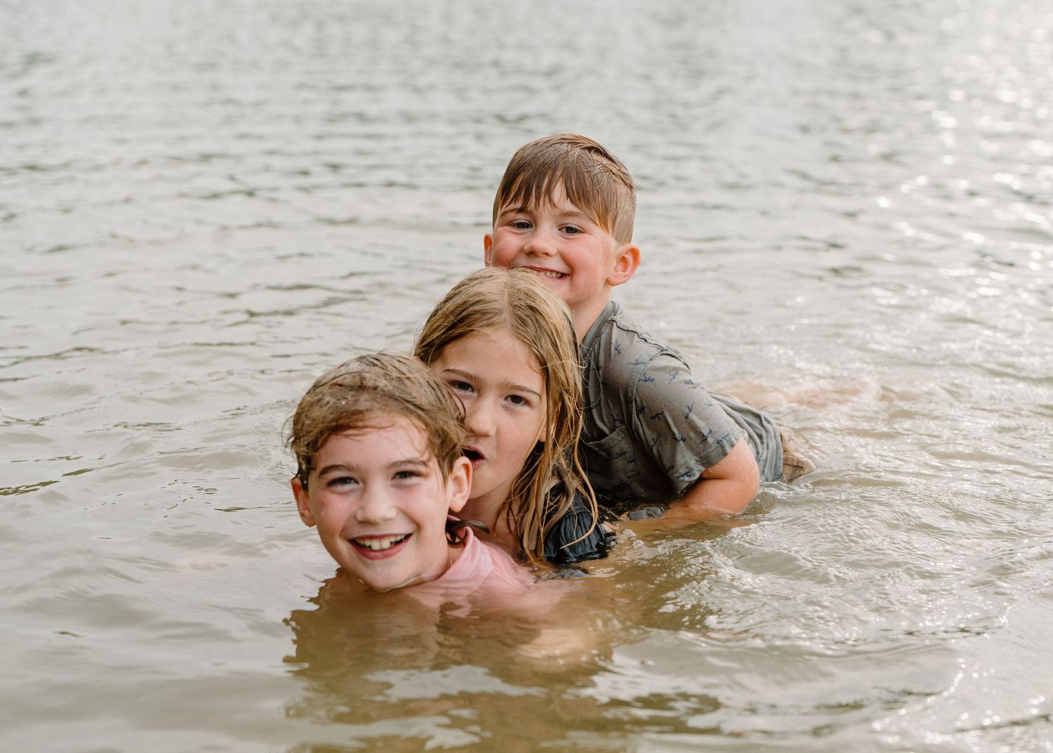 Three happy children play and smile together while swimming in a lake outdoors.