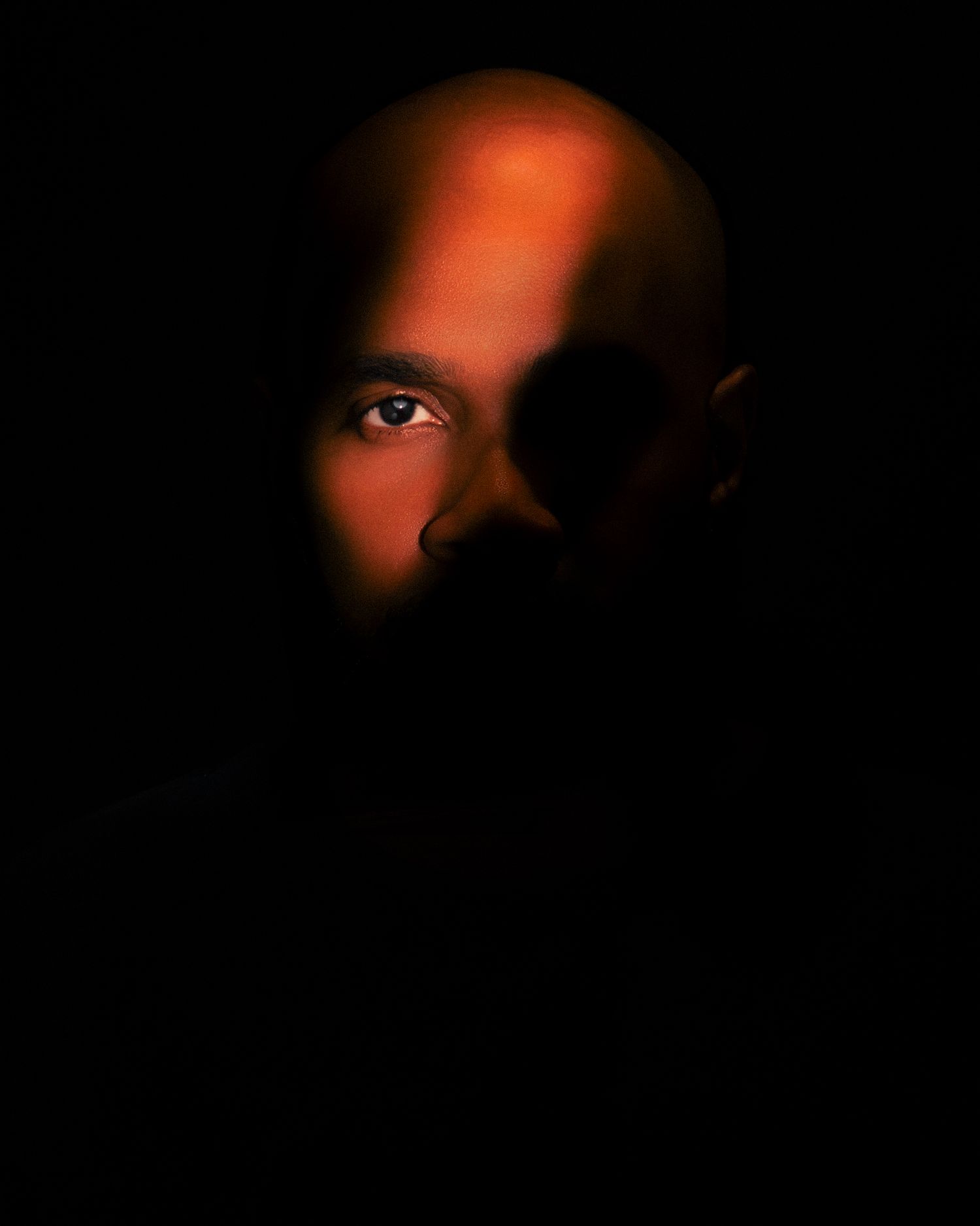 A bald man dramatically lit in warm orange cinematic light against a dark black background captured by Atlanta portrait photographer