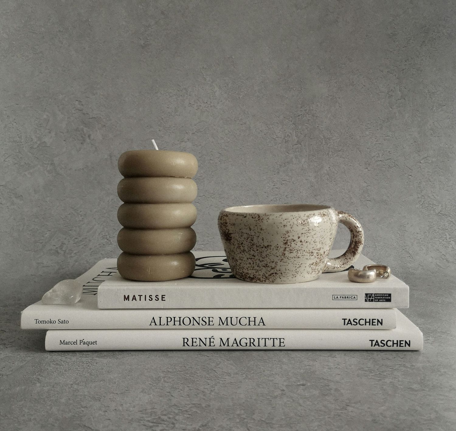 Stack of Matisse, Alphonse Mucha, and Rene Magritte Taschen books with a speckled ceramic mug and stacked donut candle.