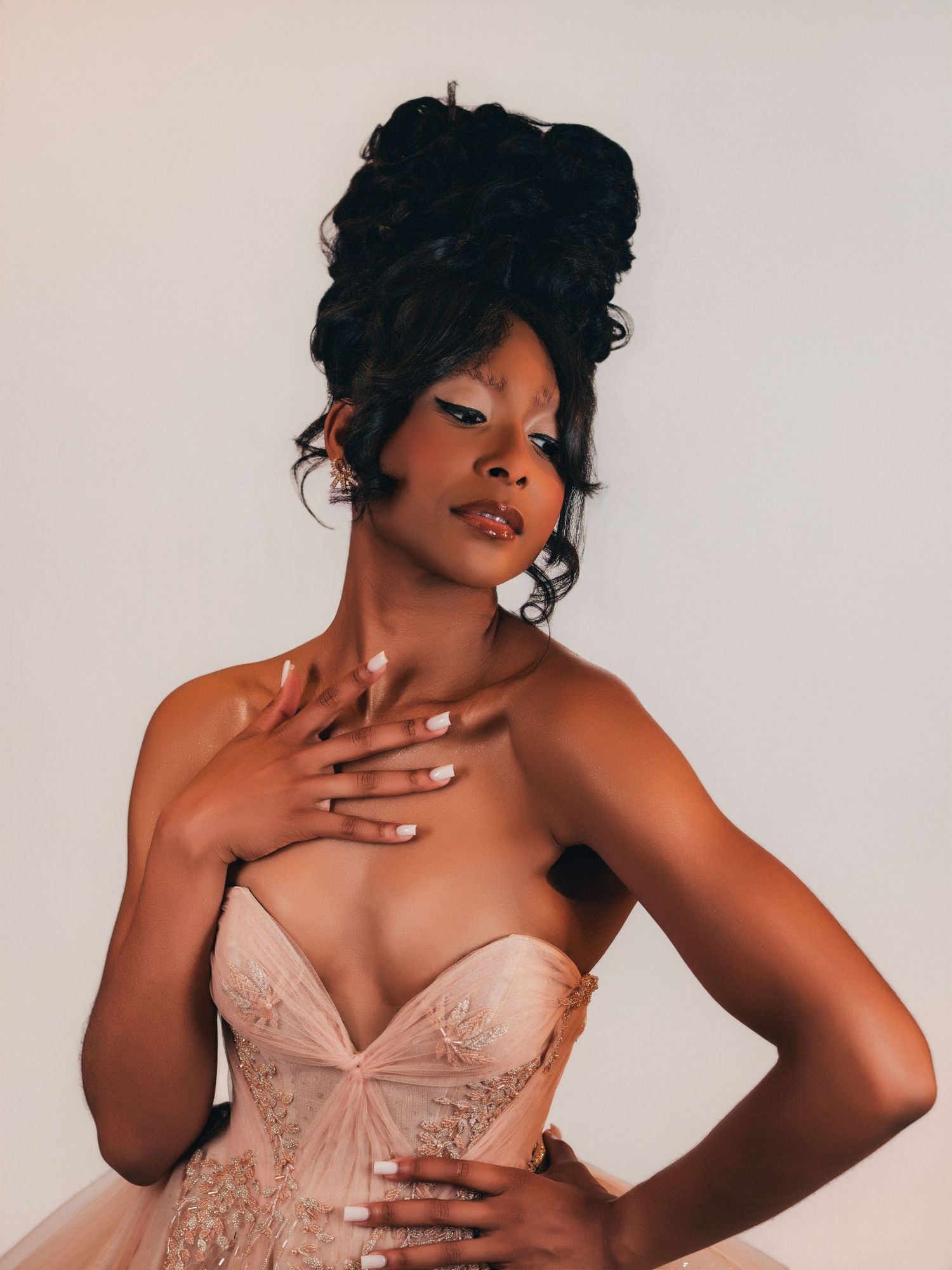 Young Black woman in elegant blush strapless corset gown with updo hairstyle posing gracefully in studio beauty portrait in Buckhead
