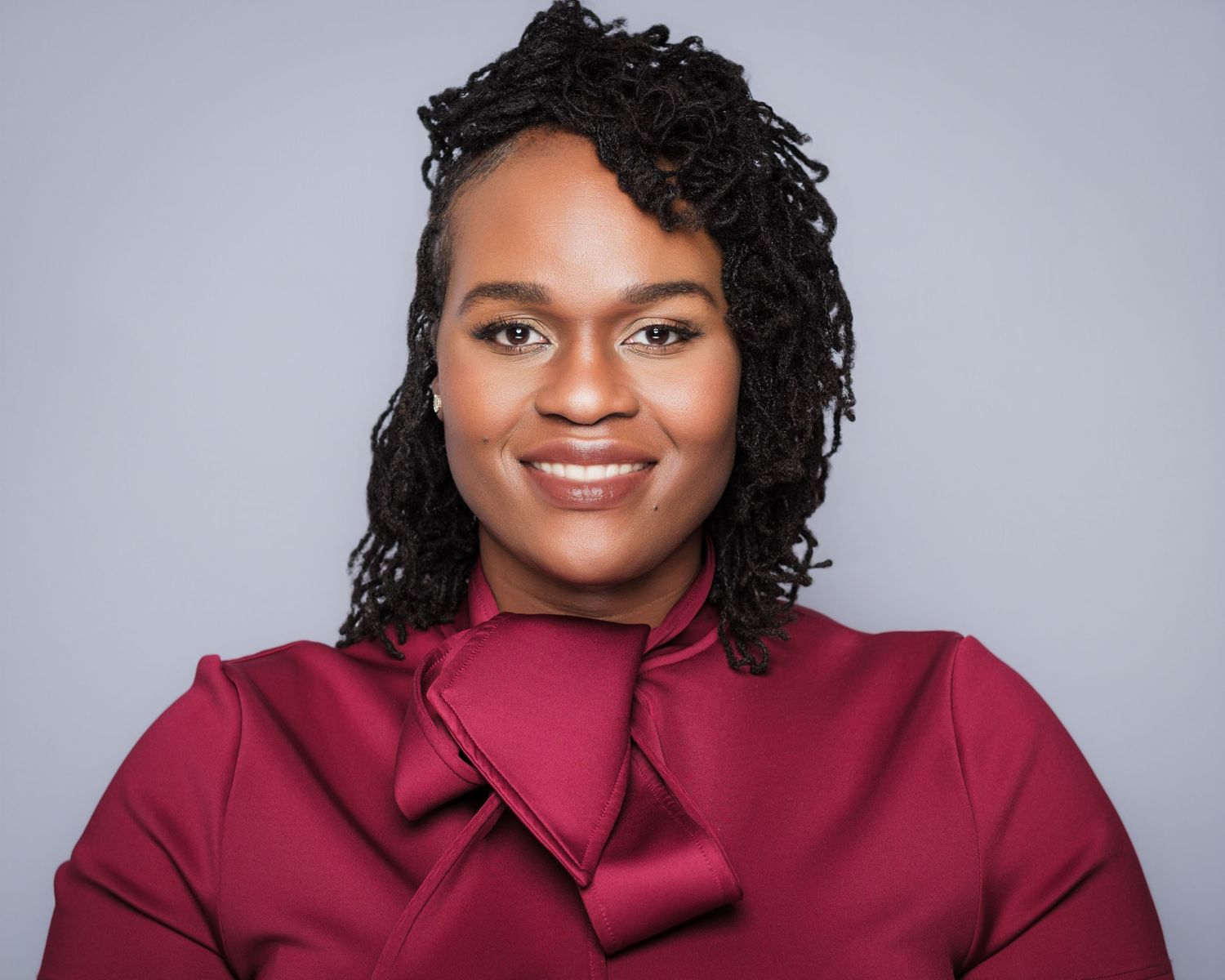 Professional headshot of a smiling Black woman with locs wearing a elegant burgundy satin blouse captured by Atlanta headshot photographer