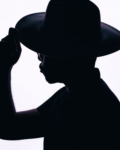 Silhouette of a person tipping a wide-brim cowboy hat against a white background.