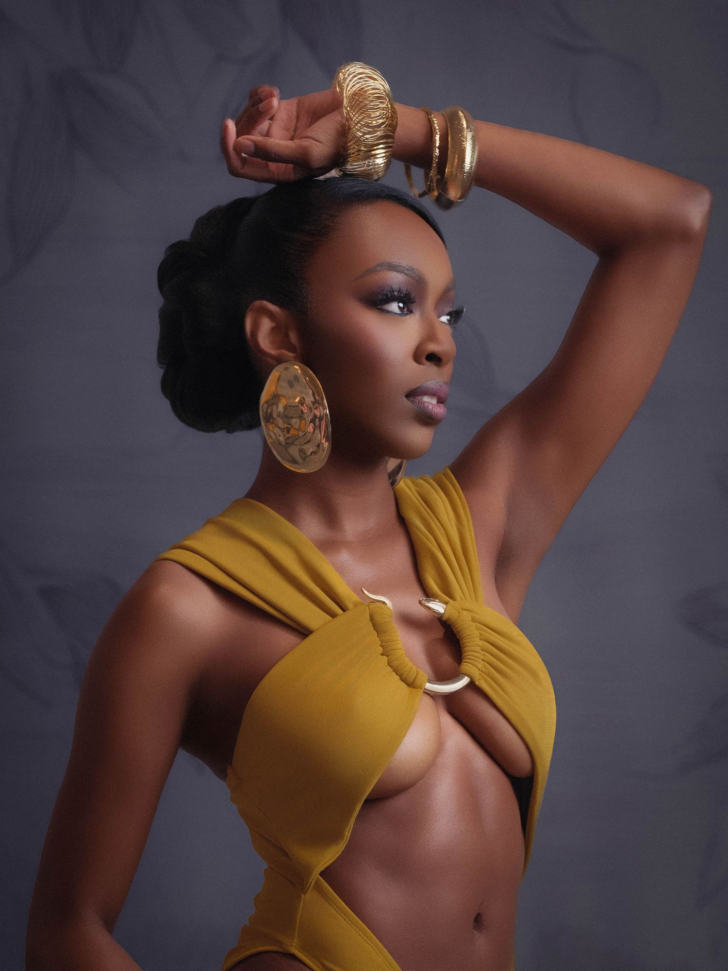 A Black woman poses in a golden yellow crop top, wearing large gold disc earrings and stacked bracelets in refined editorial in Smyrna