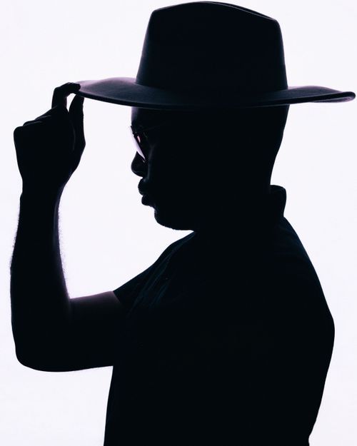 Silhouette of a person tipping their wide-brim fedora hat against a white background.