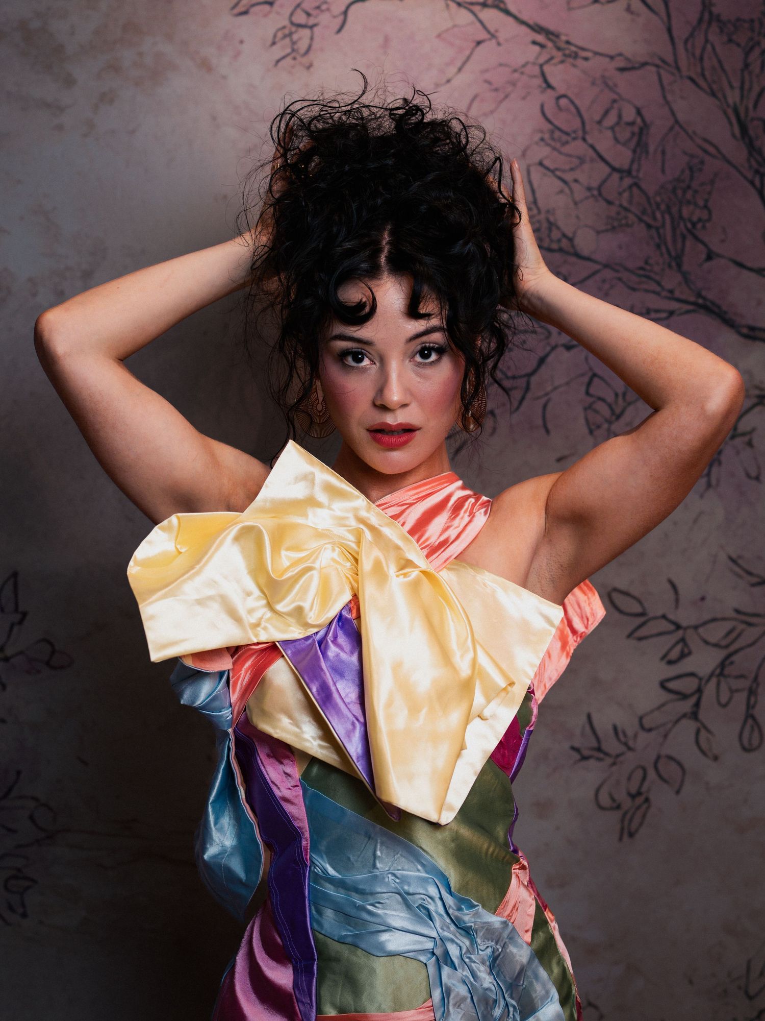 Woman in colorful satin patchwork dress with curly updo poses against floral textured backdrop in beauty portrait in ATL