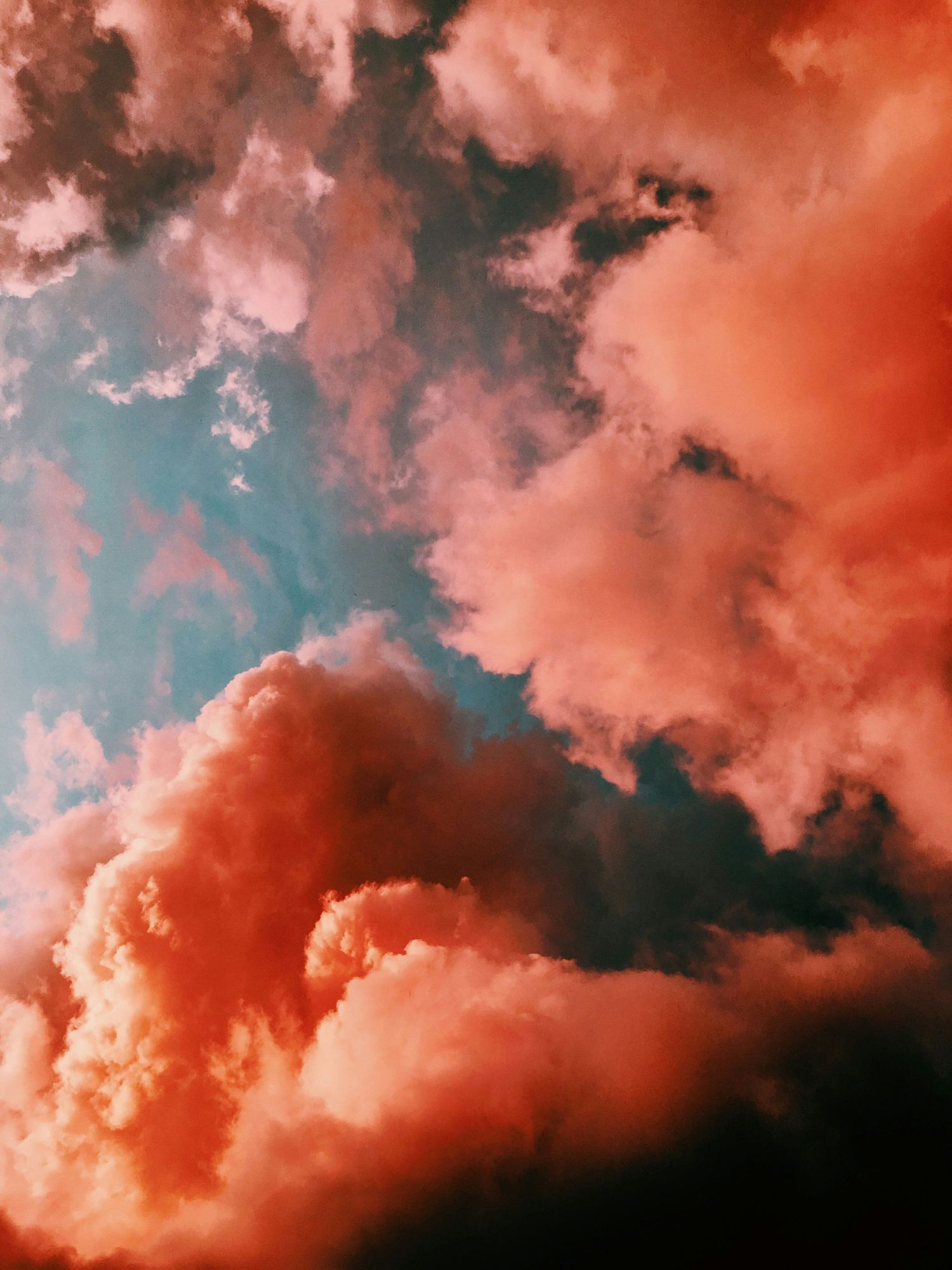 Dramatic sunset sky with vivid orange and pink cumulus clouds against a teal blue background.