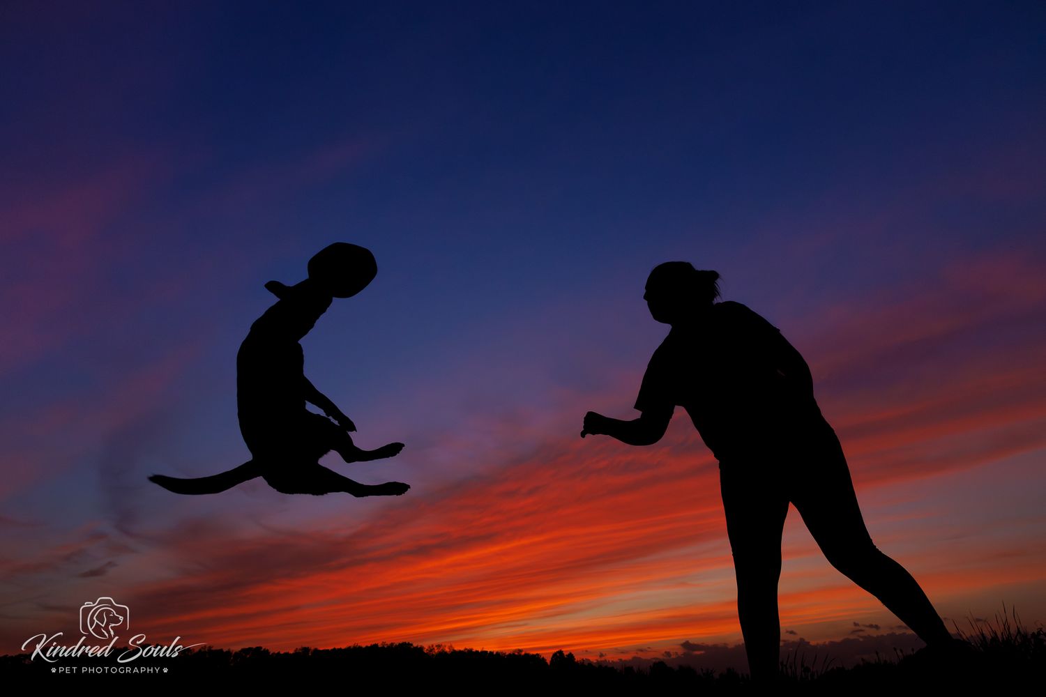 Silhouettes of two people at sunset, one airborne in a dynamic jump, against a vivid orange and blue sky.