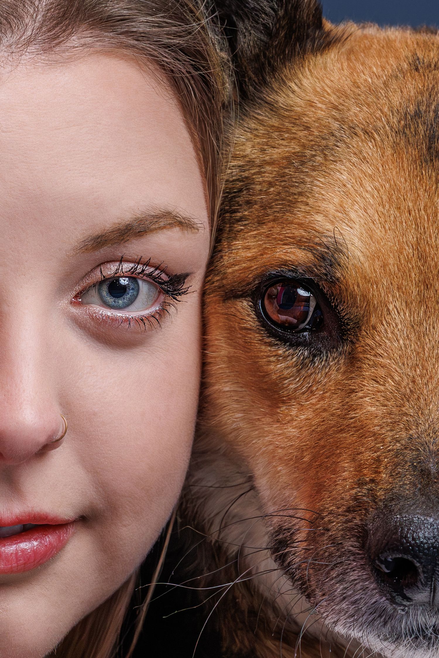 Close-up portrait of a young woman with blue eyes beside a brown dog, both facing the camera side by side.
