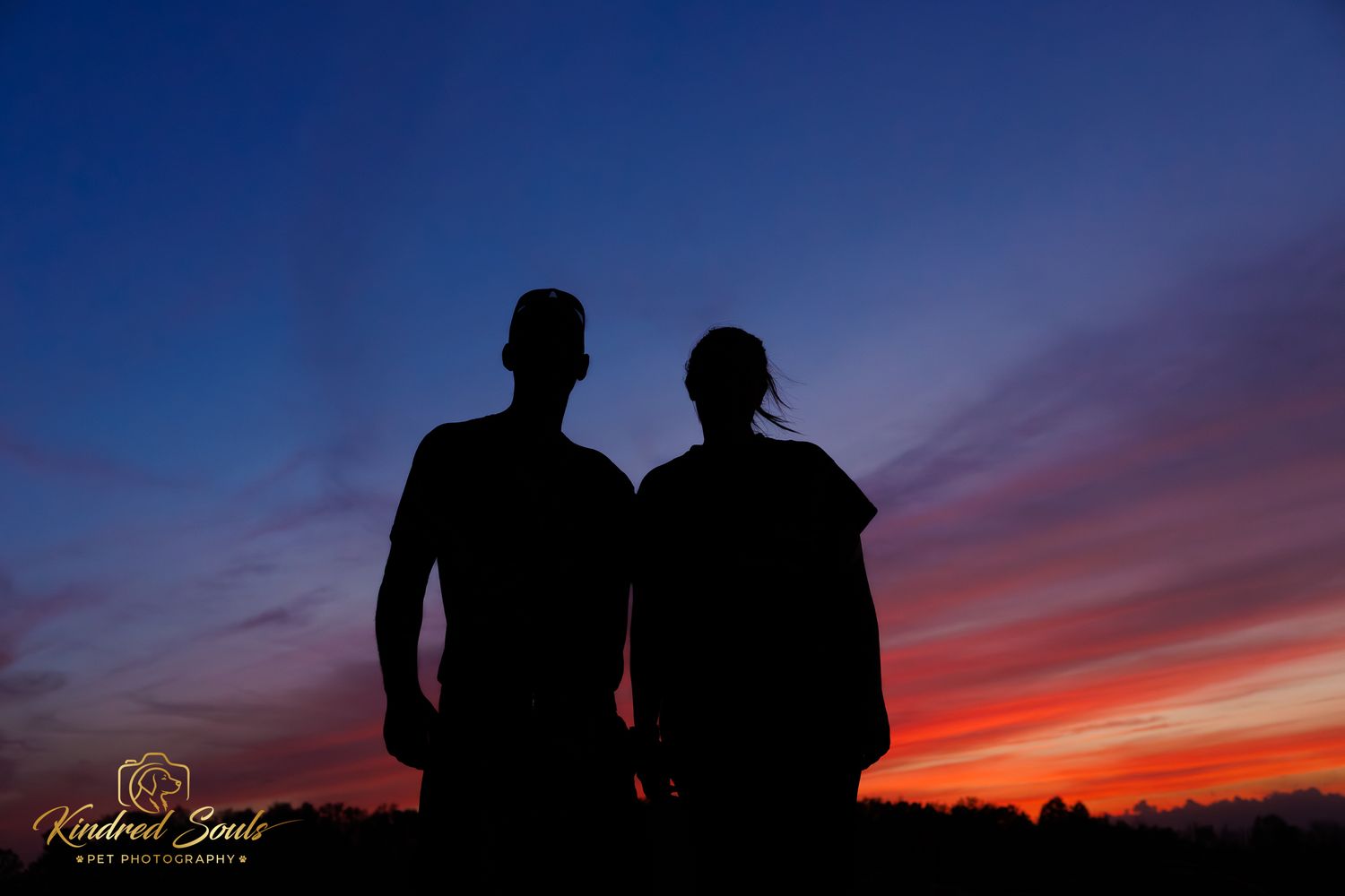 Silhouette of a couple standing together against a vibrant red and blue sunset sky.