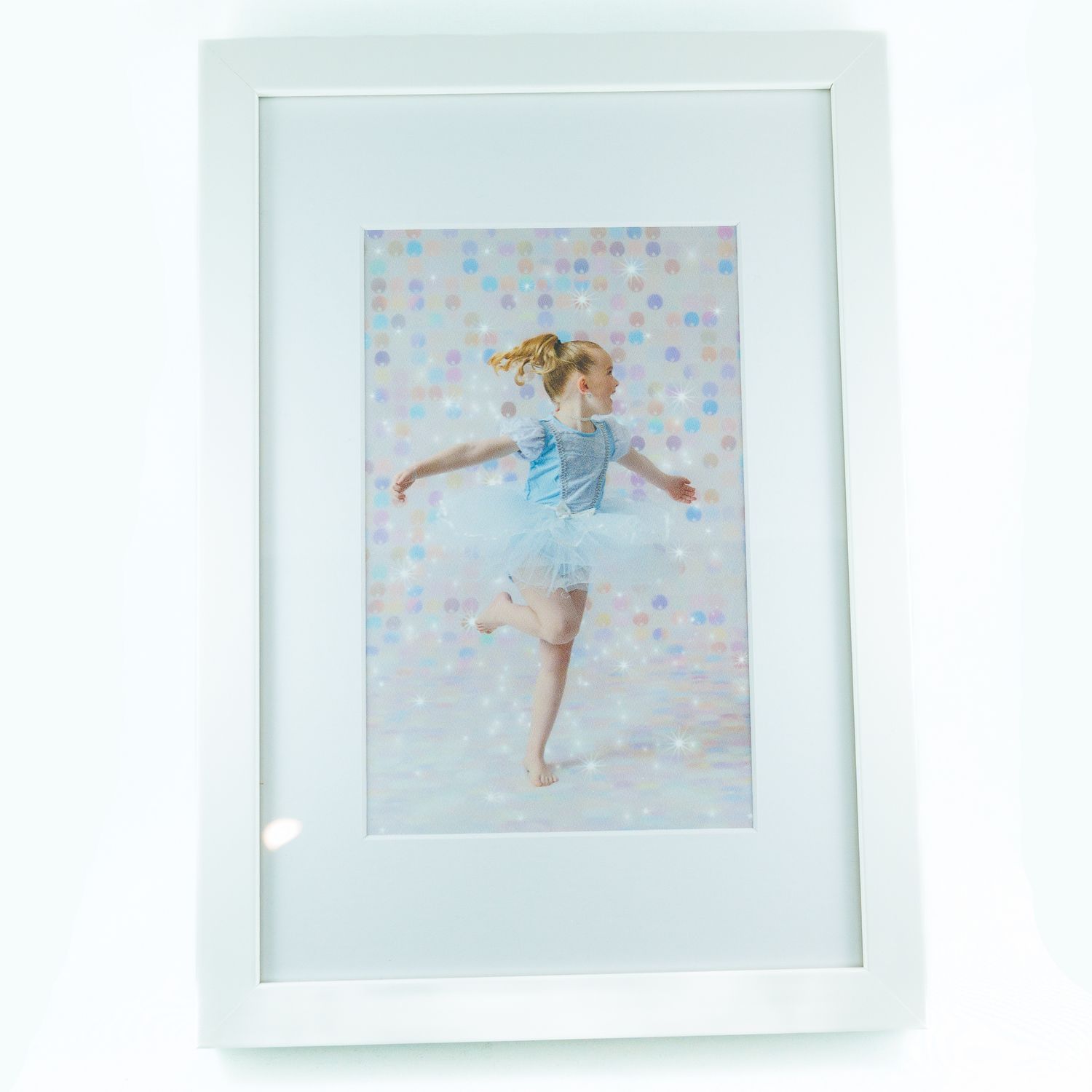 White framed photo of a young girl in a blue ballet outfit dancing gracefully against a colorful polka dot background.