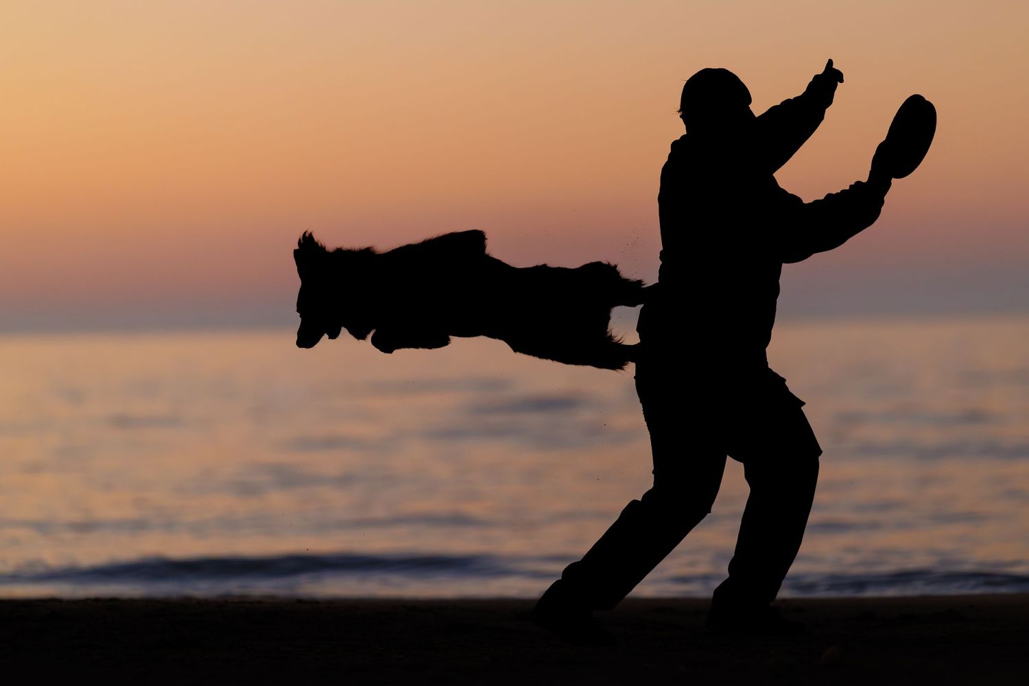 Silhouette of two people practicing martial arts on a beach at sunset with ocean in the background.