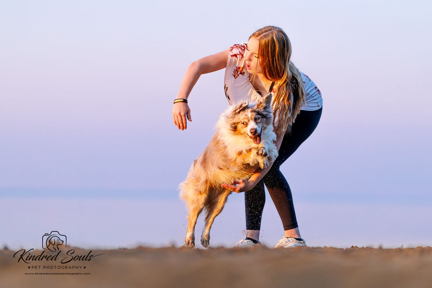 Girl hugging her Australian Shepherd dog on a beach at sunset, captured by Kindred Souls Pet Photography.