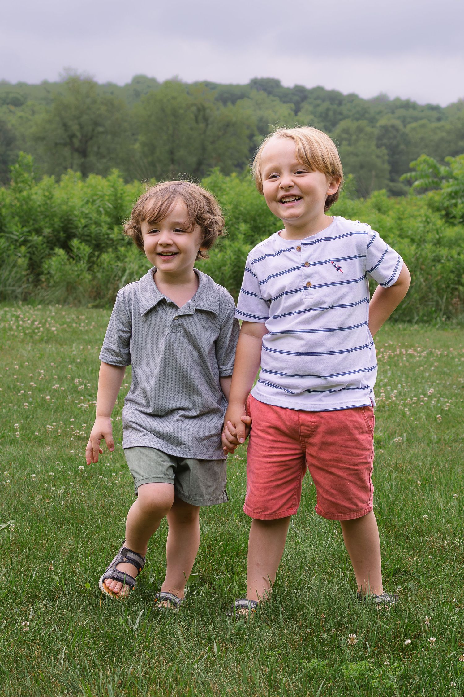 Two happy young boys holding hands and smiling together in a green grassy field.