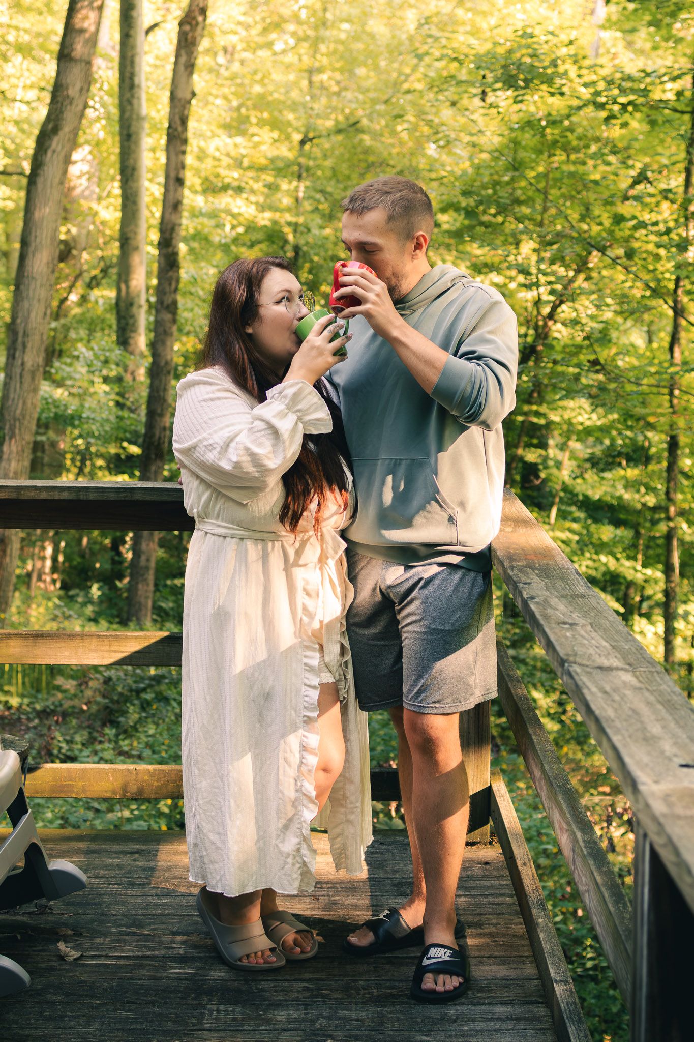 Couple sharing drinks on a wooden bridge surrounded by lush green forest trees.