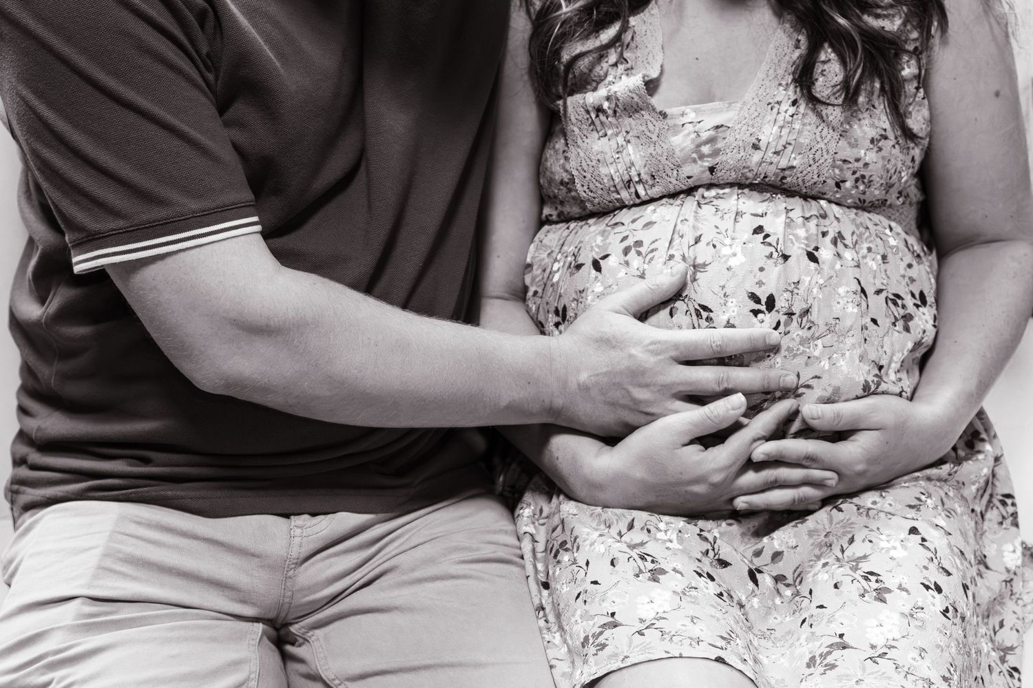 Black and white photo of a couple tenderly holding a pregnant belly together.