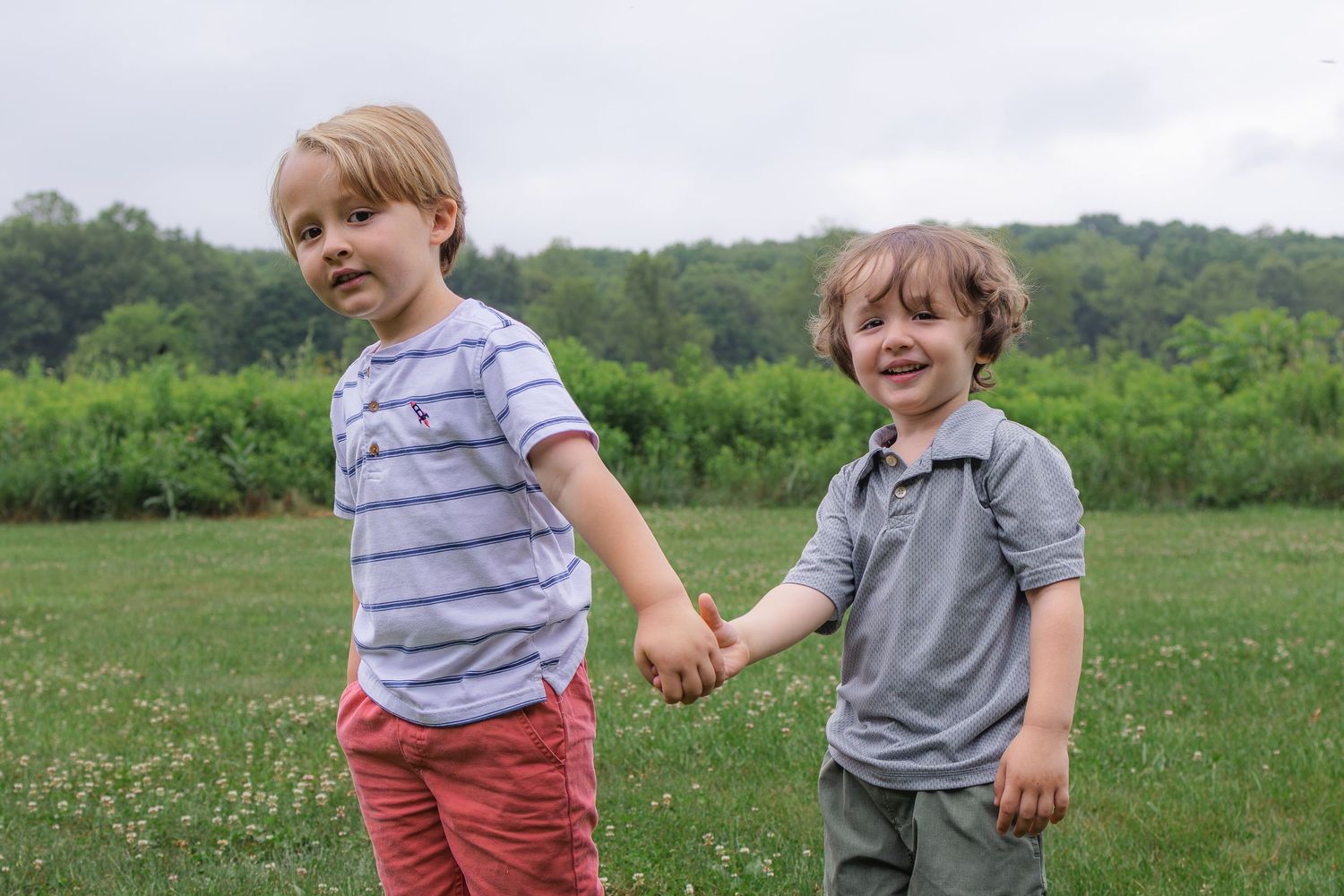 Two young boys holding hands while walking together in a green meadow.