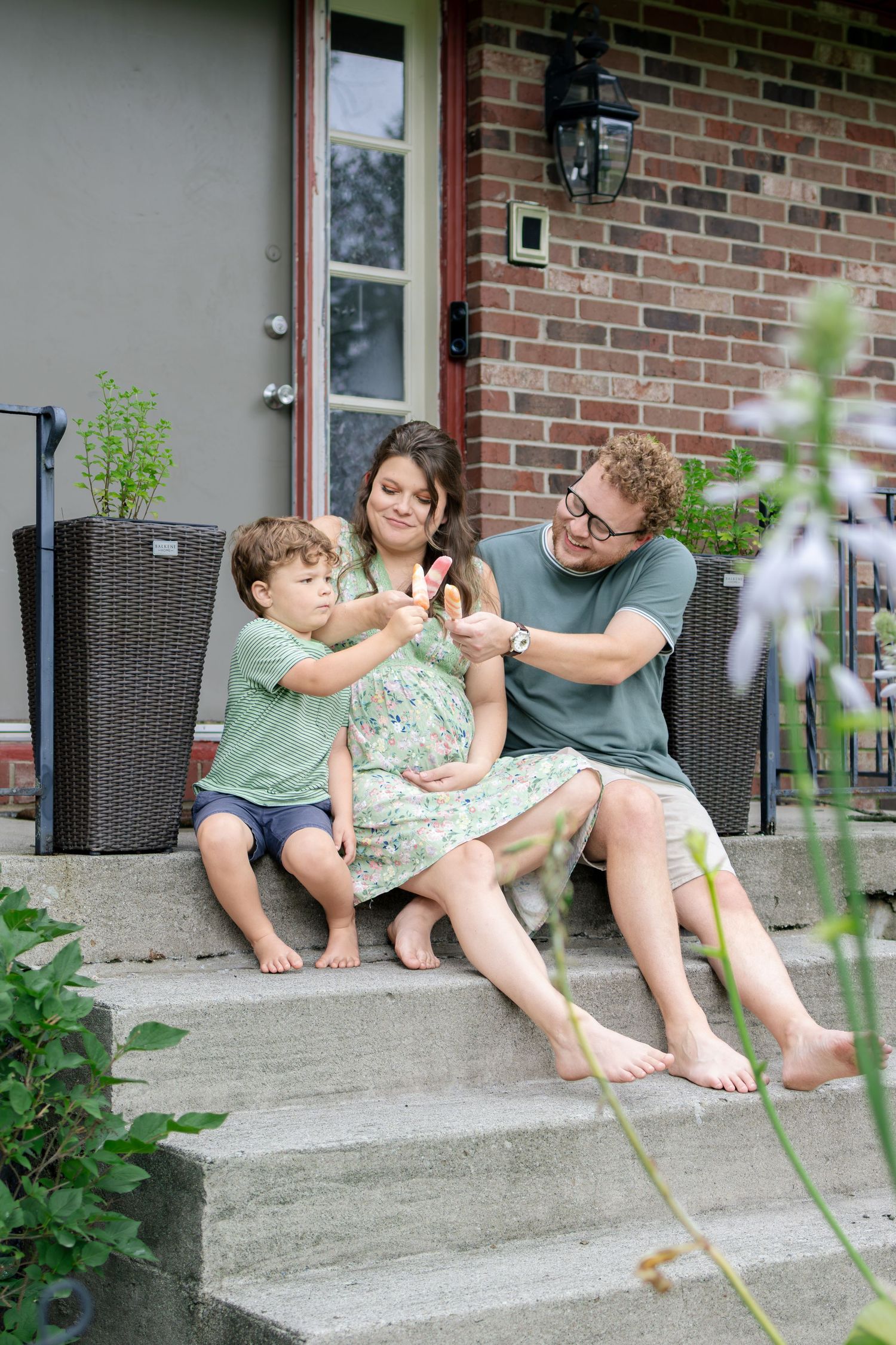 A happy family sitting on front porch steps, parents and toddler sharing a joyful moment.