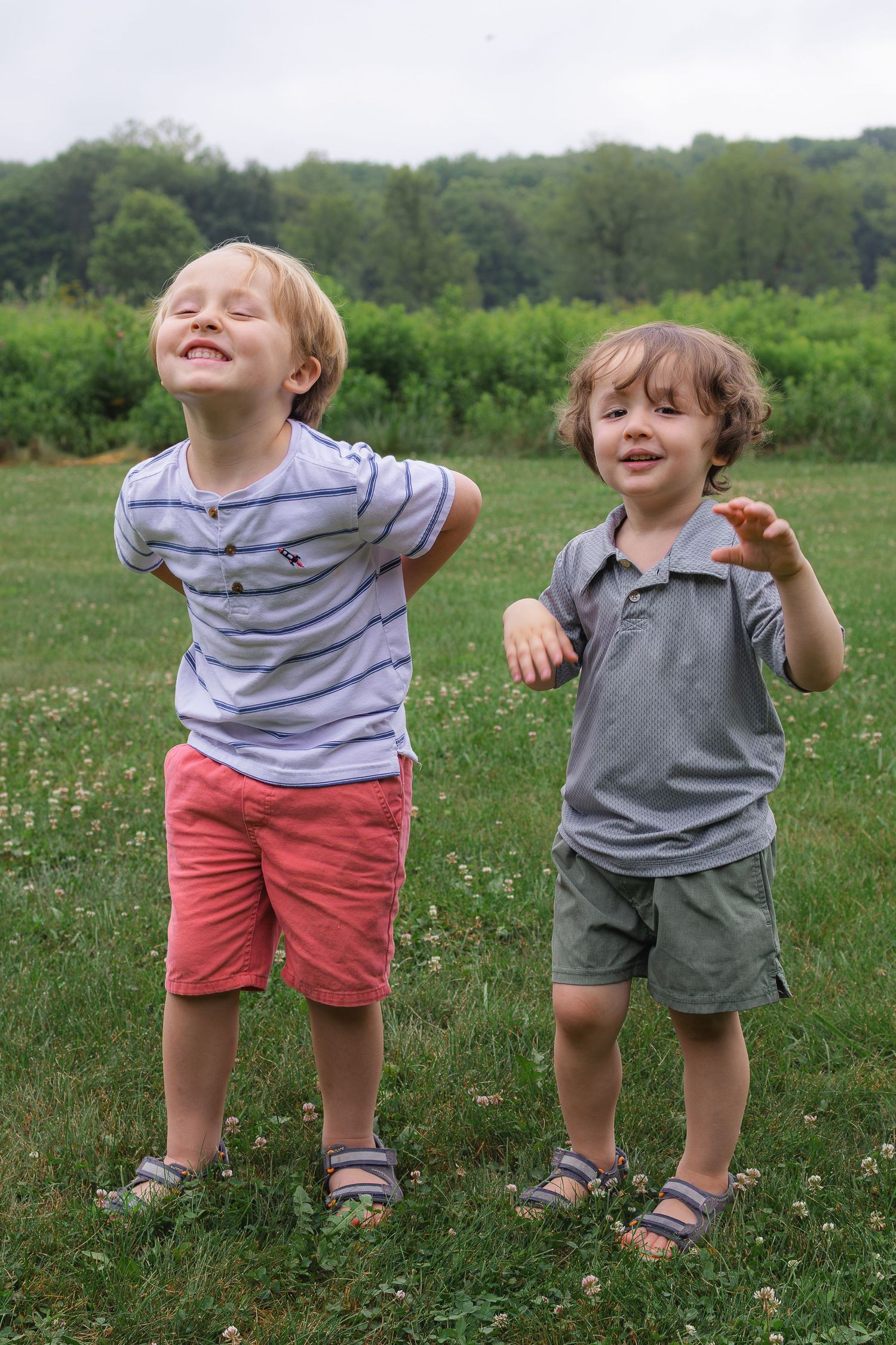 Two happy young boys laughing and playing together on a green grassy field.