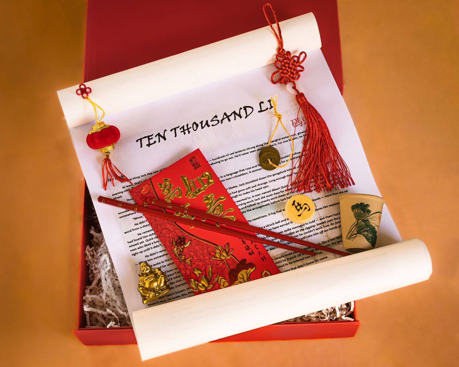 Red gift box holding an unrolled parchment scroll titled Ten Thousand Li, with a red envelope, chopsticks, tassels and a small charm.