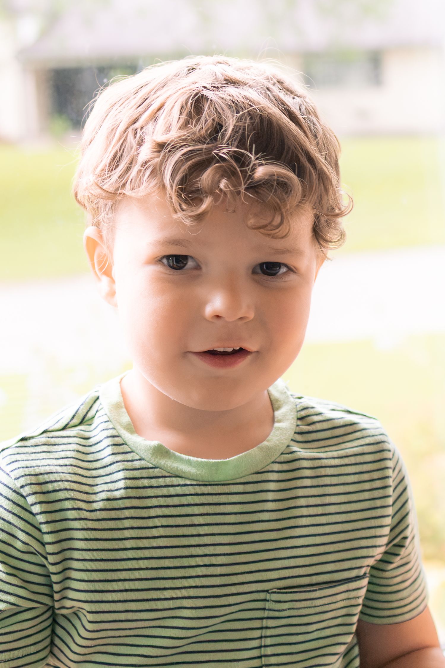 Portrait of a young curly-haired toddler boy in a striped shirt outdoors.