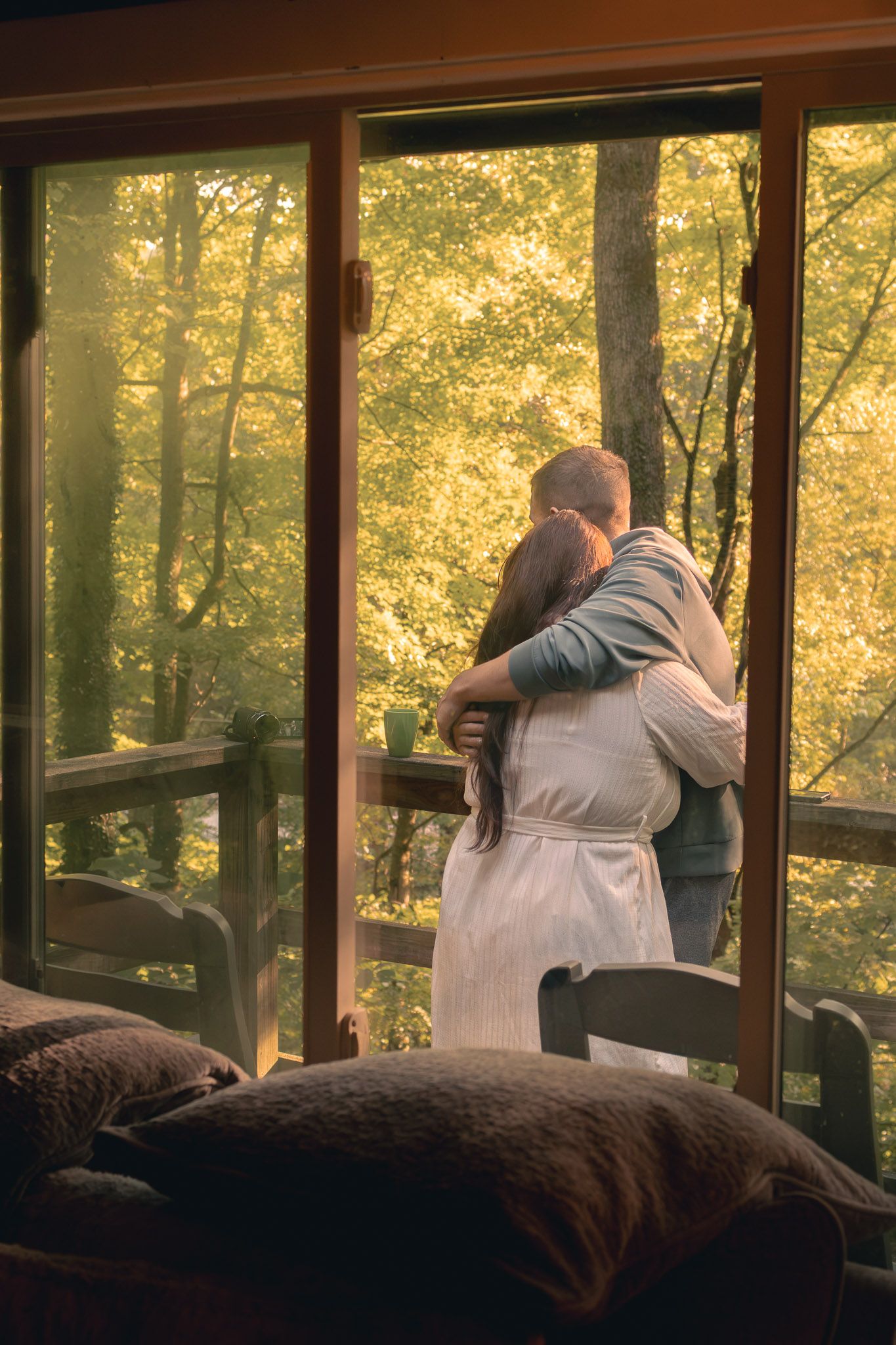 Couple embracing on a cabin balcony with vibrant autumn forest views through large glass doors.