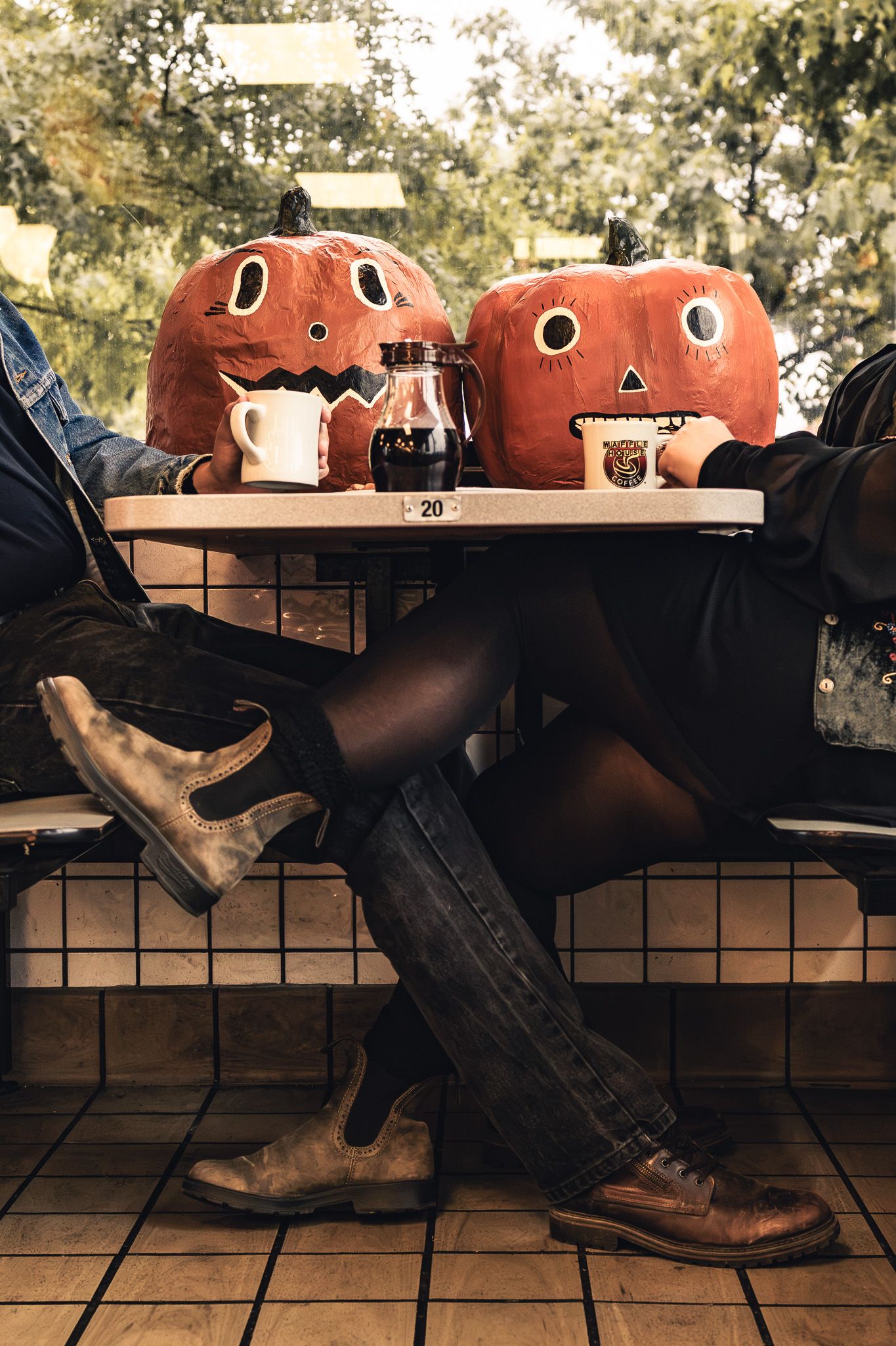 Two people with jack-o-lantern heads sitting at a cafe table with coffee drinks for a Halloween photo.