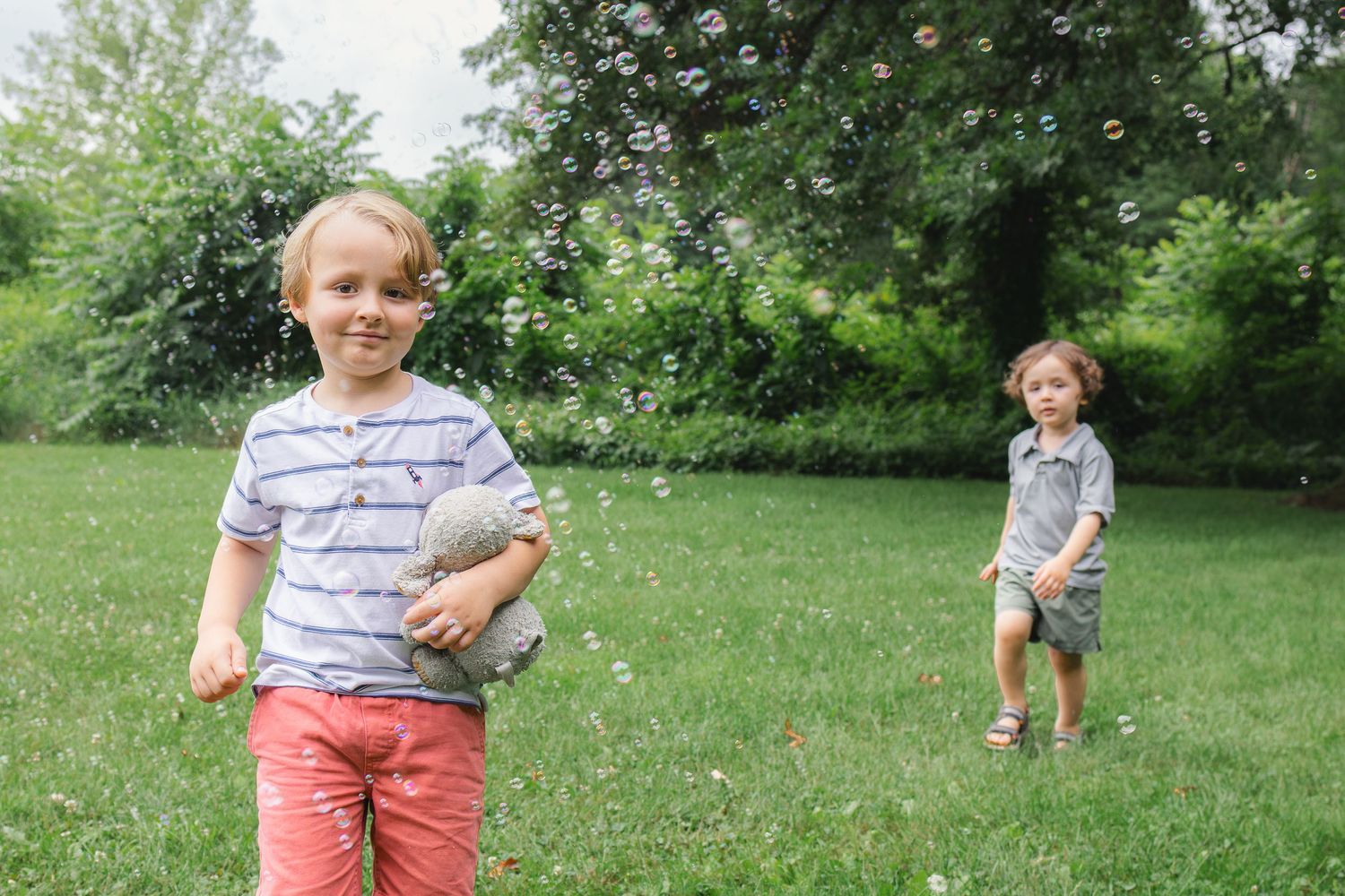 Two young boys playing with bubbles in a lush green park on a sunny day.