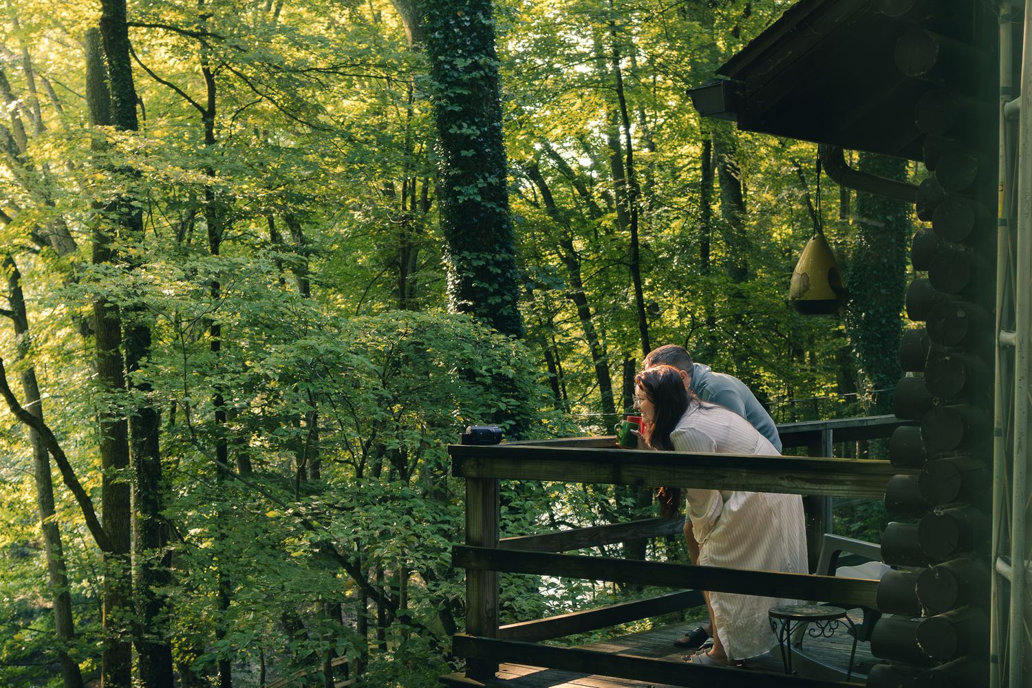 Couple sharing a romantic moment on a wooden cabin porch surrounded by lush green forest trees.