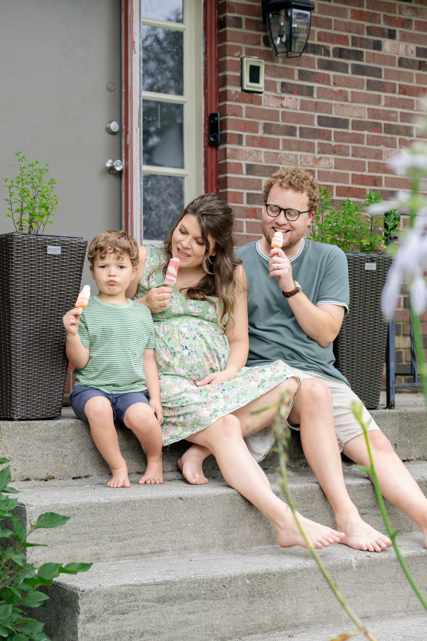 A cheerful family of three enjoying popsicles together on their front porch steps.