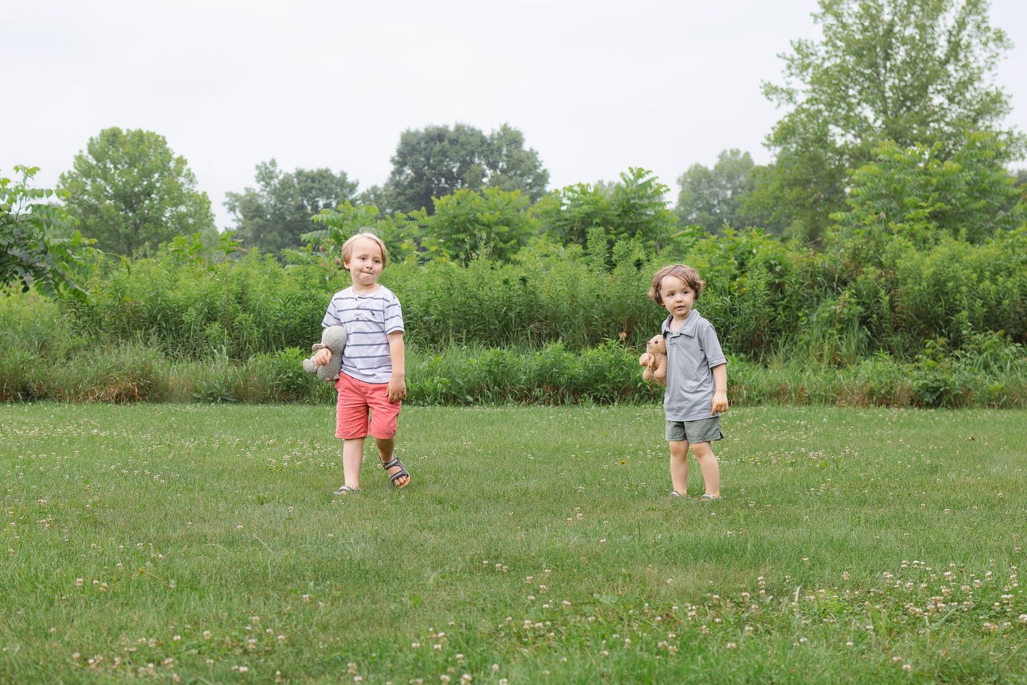 Two young boys standing apart in a wide green grassy field on an overcast day.