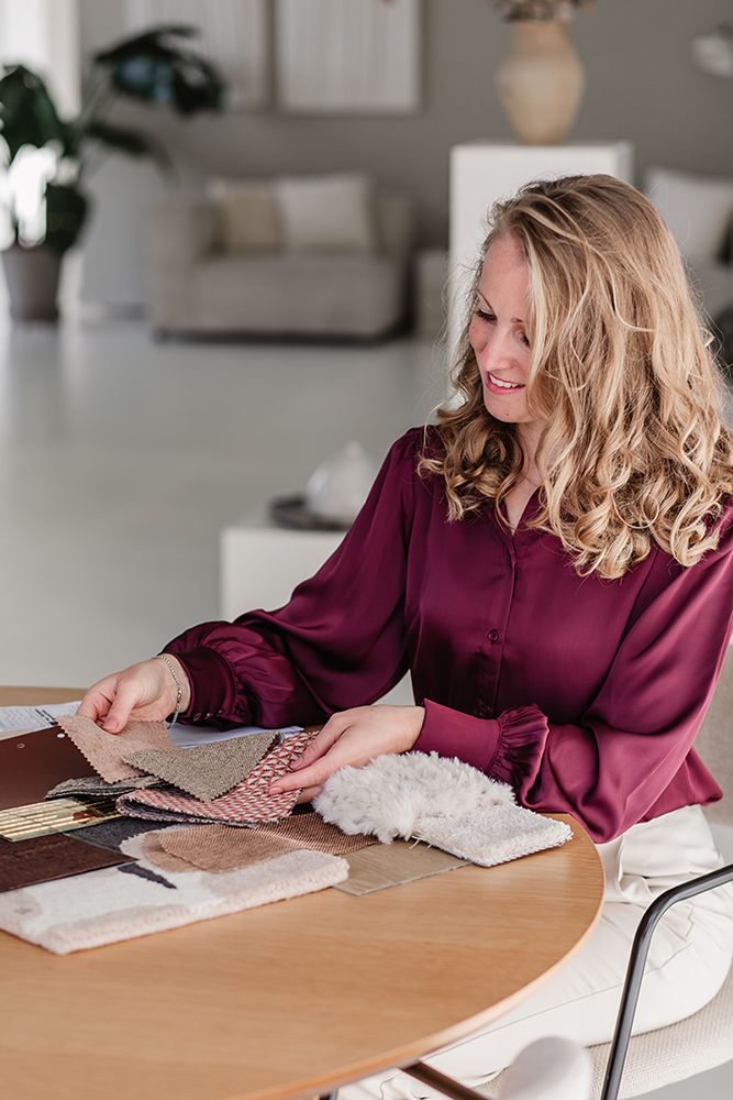 Personal branding shoot voor een interieur styliste. Op een lichte locatie en met kleur in de kleding. Op tafel liggen staaltjes.