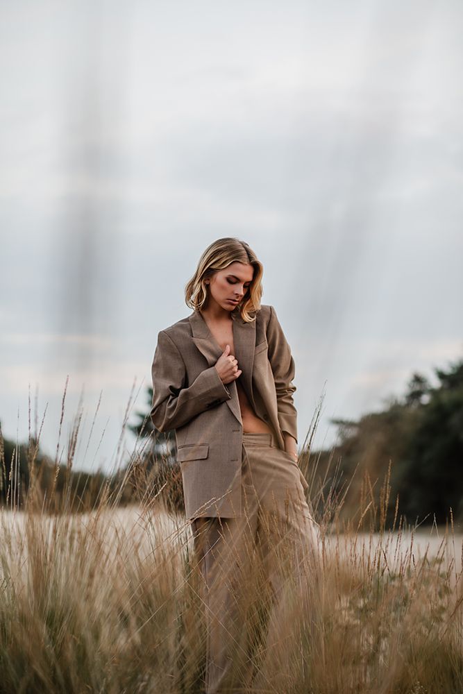 Foto van een vrouw in de natuur met een lichtbruin pak aan in de Drunense Duinen.