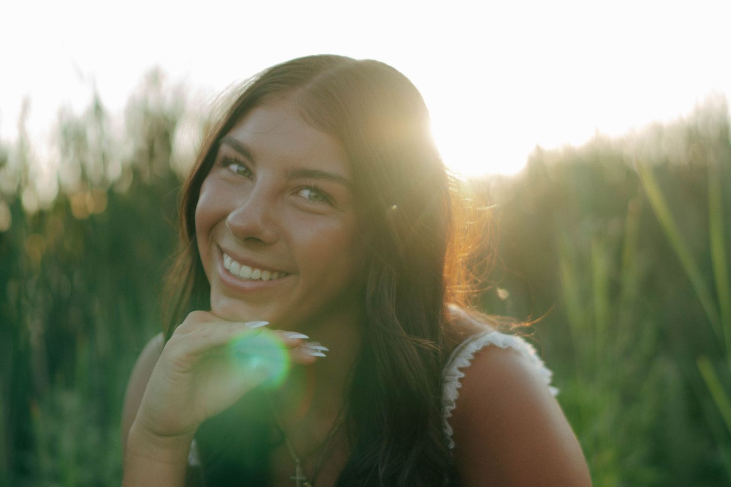 Beautiful smiling brunette woman in golden sunlight with lens flare in green field.