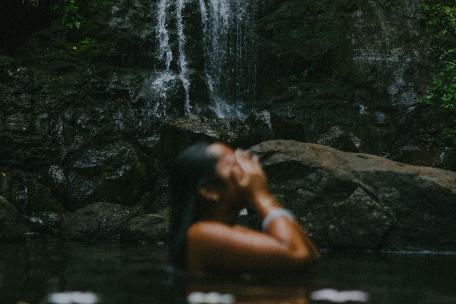 Woman bathing in natural pool near waterfall in lush tropical setting.