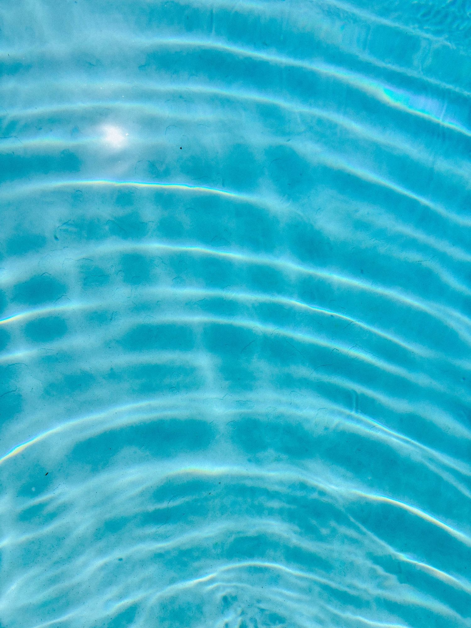 Close-up of rippling turquoise pool water with light reflections creating curved wave patterns.