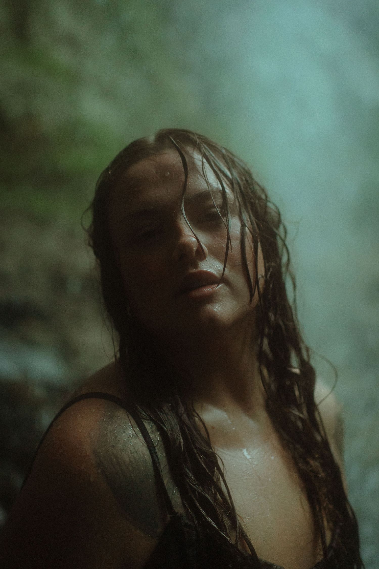 A woman with wet hair stands in misty forest light, water droplets on her skin, in a moody outdoor portrait.